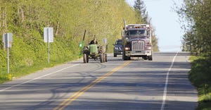 tractor driving down road being follow by semitruck