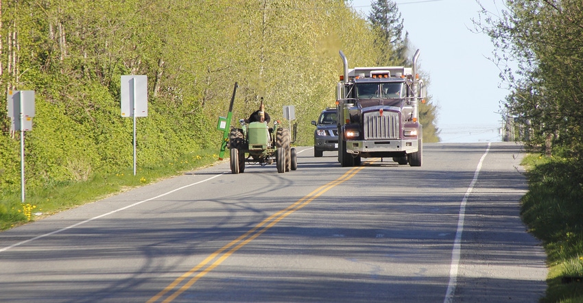 tractor driving down road being follow by semitruck