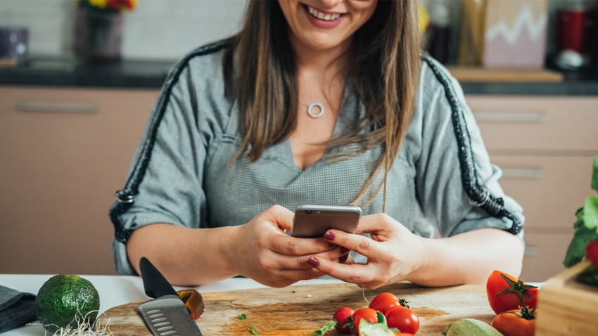 woman making salad and texting