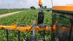 A sprayer applying fertilizer to a cornfield at V4-V5 stage