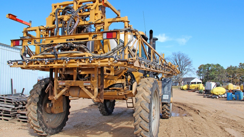 Close up of a yellow ground rig sprayer sitting in a shop lot.
