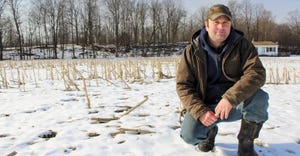 Farmer Jon Lucas kneels in the snow of a corn field