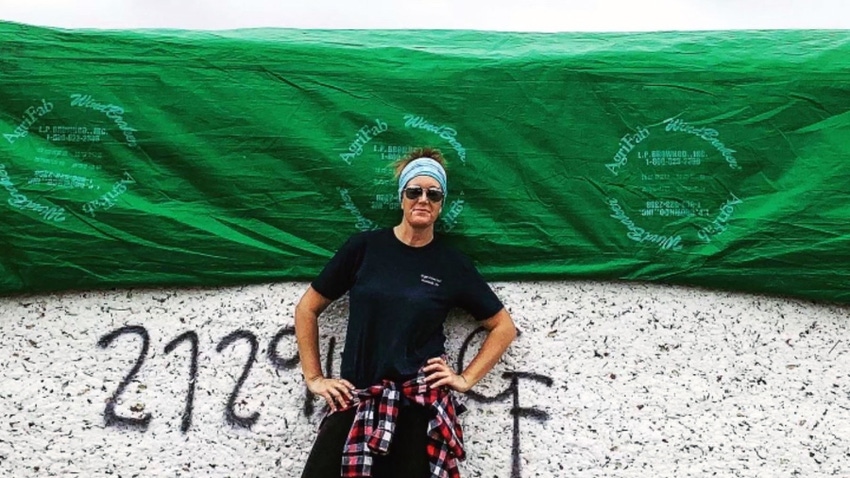 Woman farmer standing in front of cotton bales, wearing sunglasses and a bandanna.