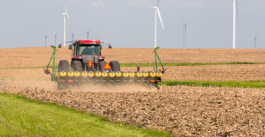 Planter working in a corn field with wind turbines on horizon