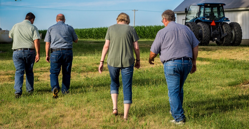 woman and three men walking away across grassy yard