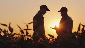 Two farmers in a field with a sunset in the background