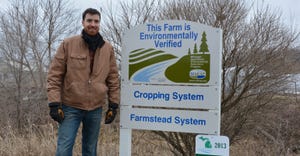 Matthew Romans  stanfing by  a sign that says this farm is enviromntally verified