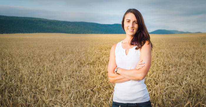 A young, smiiling female farmer poses in a middle of a field with arms crossed