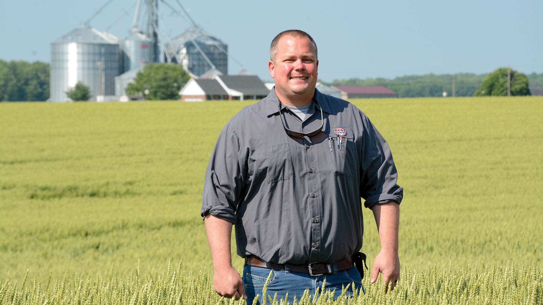 Farmer standing in wheat field with grain setup in background.