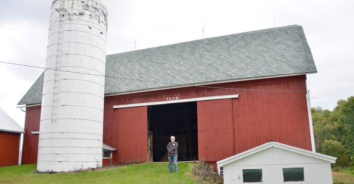 John Mills stands in front of barn he is repairing