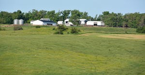 farmstead of white buildings on horizon of lush green farmland