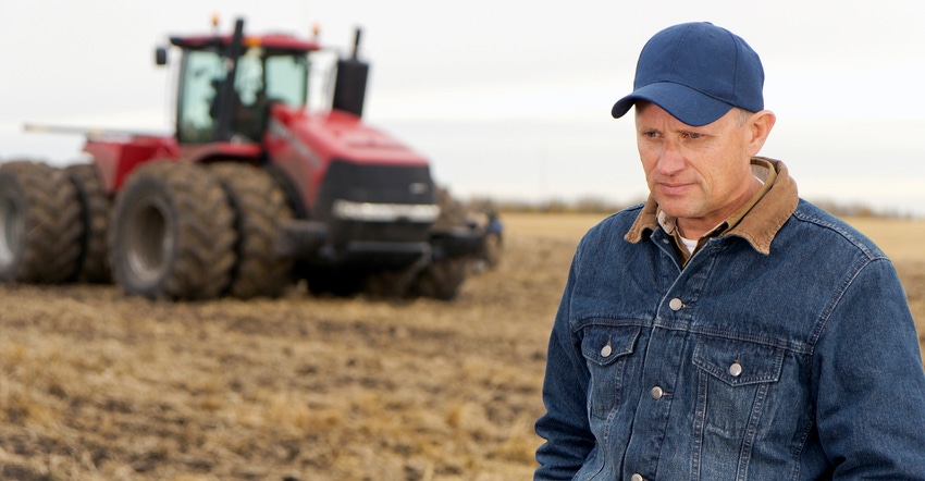 farmer looking sad in field with tractor in the background