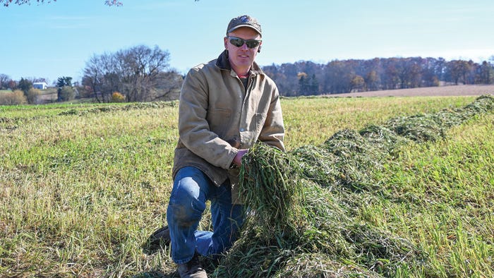 William Thiele kneeling in a field holding cover crops in his hands