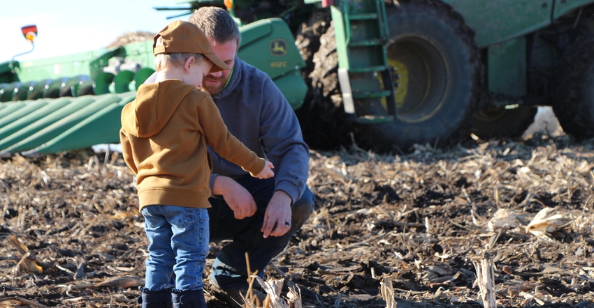 farmer with his young child in field crouching in front of a combine