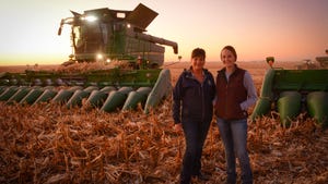 Julie and Bridjet Blout standing in a harvested cornfield with a combine in the background