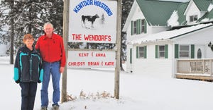 Kent and Anna next to their sign " Kentdor Holsteins" on their farm