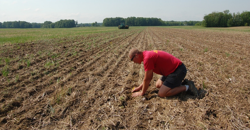 Roger Wenning, Greensburg, Ind., kneeling on ground in planted field to determine planting depth