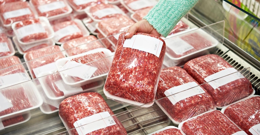 Woman in a grocery store picking up a package of ground beef from a freezer