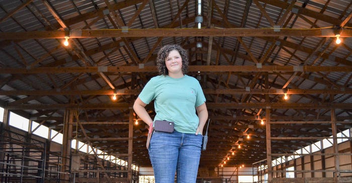 A young lady standing inside of a cattle barn and posing with her hands in her pockets