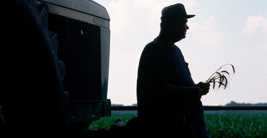 silhouette of farmer holding stems by tractor