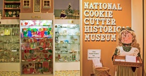 Interior of a cookie cutter museum with glass cases filled with artifacts and cookie cutters and a wooden doll holding a box 