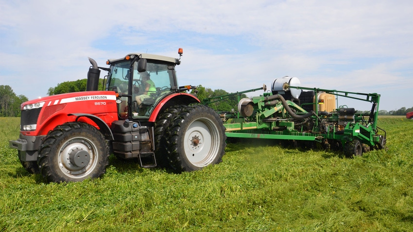 A red tractor and green planter planting into green cover crops