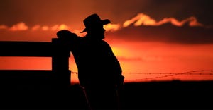 silhouette of rancher leaning against fence
