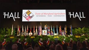 A stage, for the the Taste of Maryland Agriculture event, decorated with various flags and florals as award nominees sit on chairs