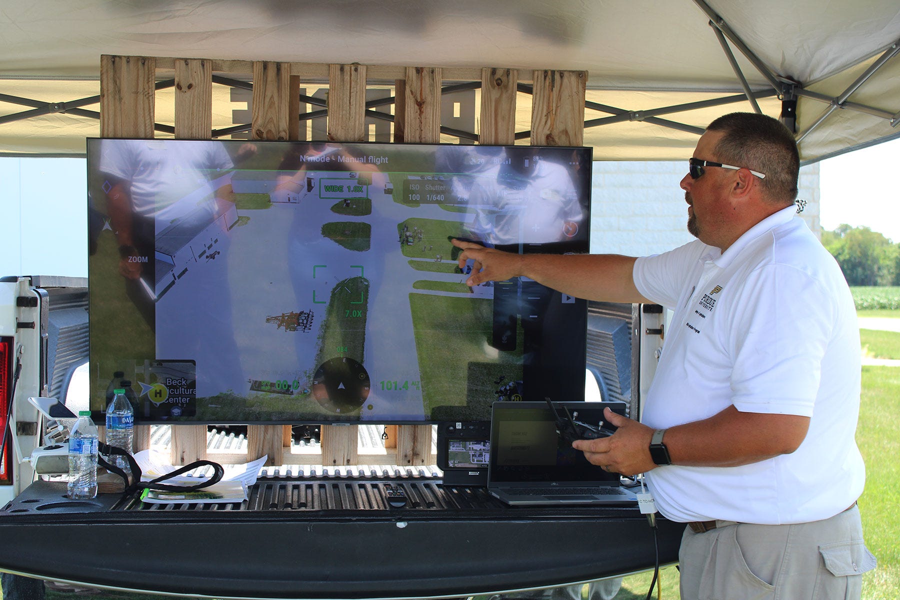 man pointing to large display monitor showing aerial view of research facility