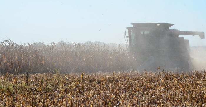 A cloud of dust surrounding a combine in a corn field