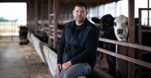 Derek Dean sitting besides cattle in barn