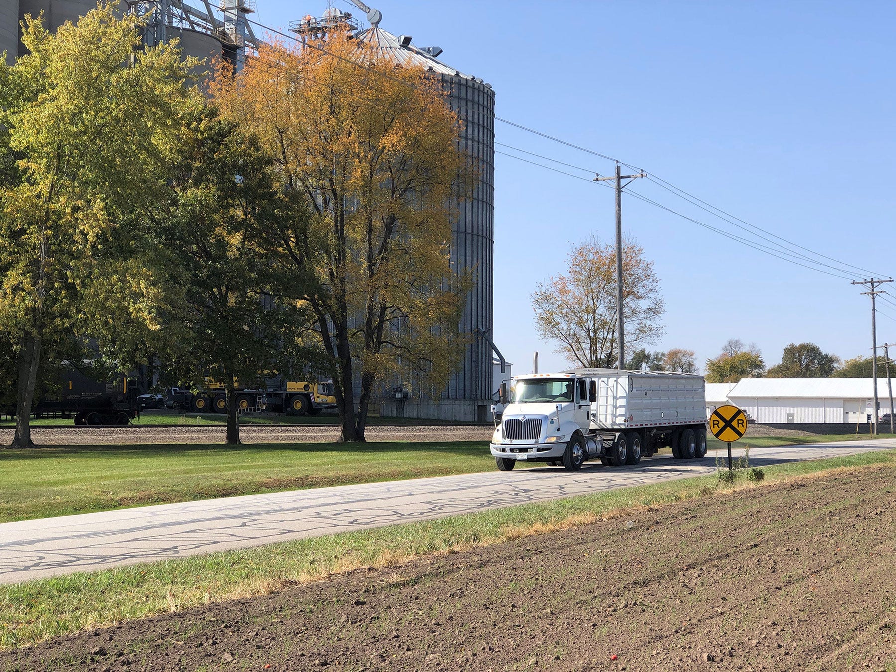 A semi tractor driving down a rural road next to a grain storage facility