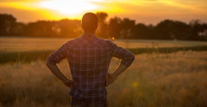 farmer standing in field at sunset