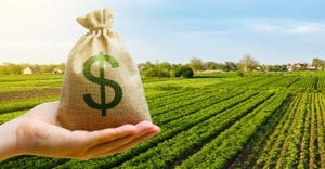 hand holding dollar money bag in front of farm field