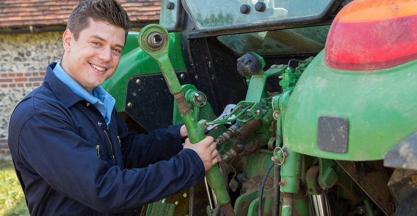 Mechanic repairing tractor. Mechanic smiling at camera. Using wrench on back of tractor.