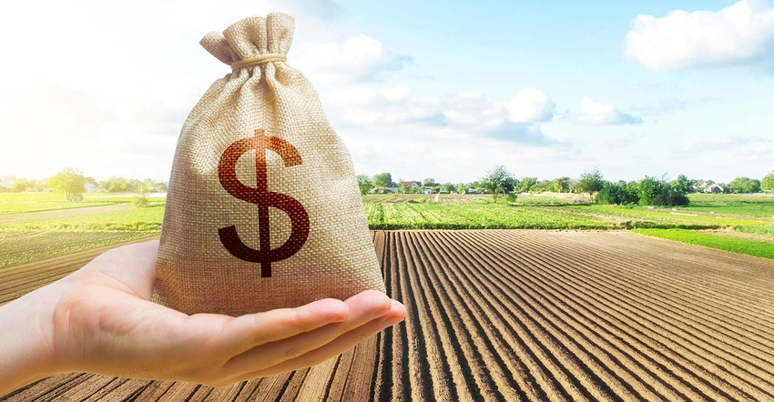 Hand holding bag of money with farm field in background
