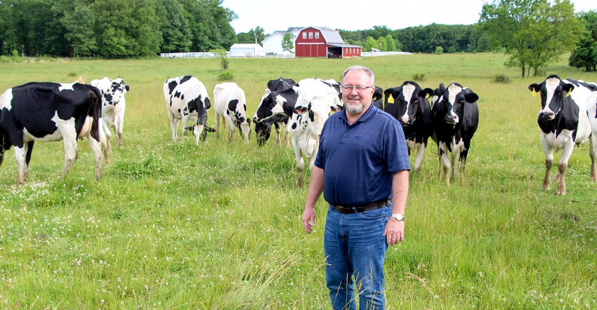 Jack Dill standing in a pasture surrounded by cows and a red barn in the background