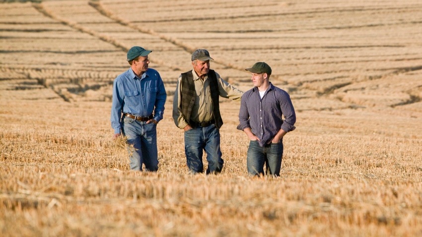 three generations of farmers walking through wheat field