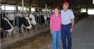 Yogi and Brian Brown standing in barn with Holstein cows in background