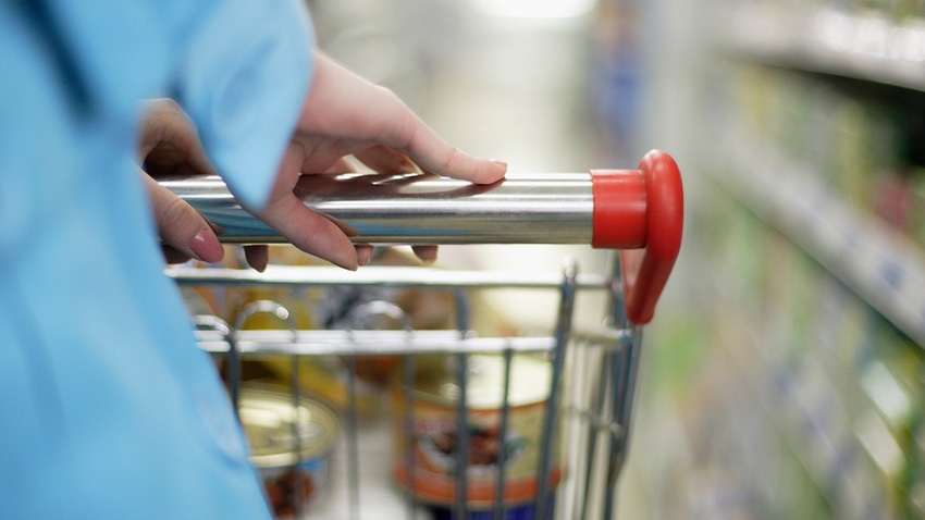 Person pushing grocery cart through food store aisle.