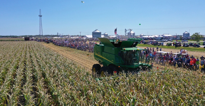 Aerial picture of John Deere combine harvesting corn while people watch from behind a rope.