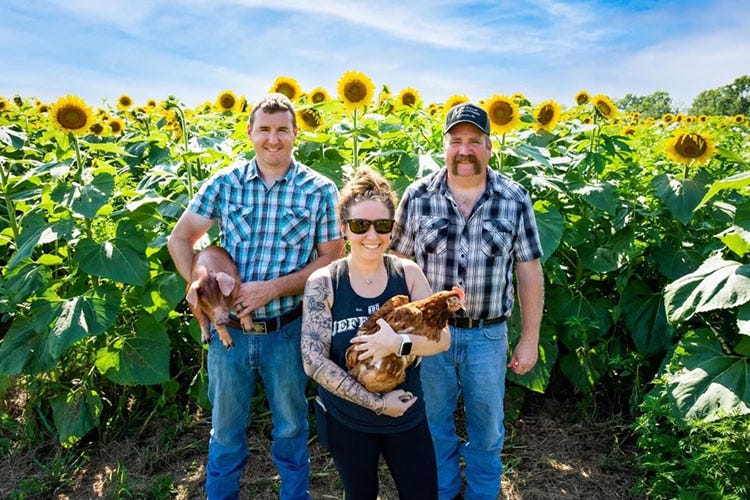 rob Salem -- Pictured from left, Nathan Hunt holding a piglet, Lindsay Baker holding a hen and Mark Boyer in front of a sunflower field 