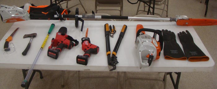 telescoping pole trimmer (top), and (from left) a small handheld saw, safety glasses, hatchet, weed wand, small chainsaw, compact saws-all, hand pruner, bypass lopper, medium-size chainsaw and protective gloves for handling herbicides