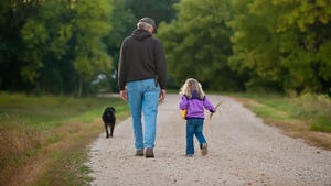 Middle-aged man, little girl and dog walking down path away from camera
