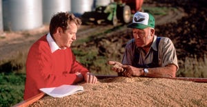 Farmer talking to banker by a wagon of soybeans in front of grain bins