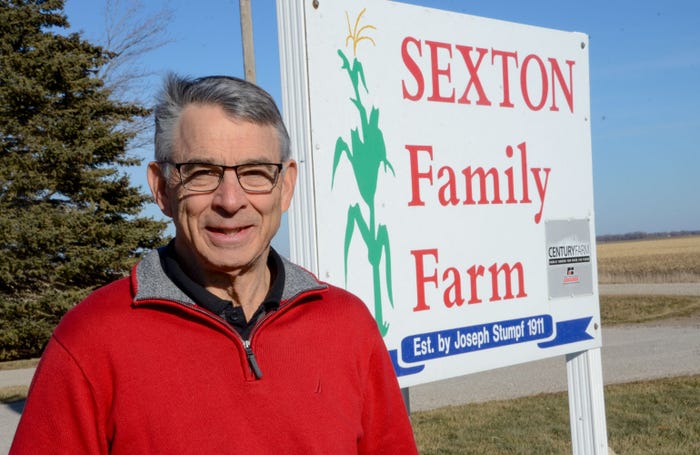 Keith Sexton stands beside Sexton Family Farm sign