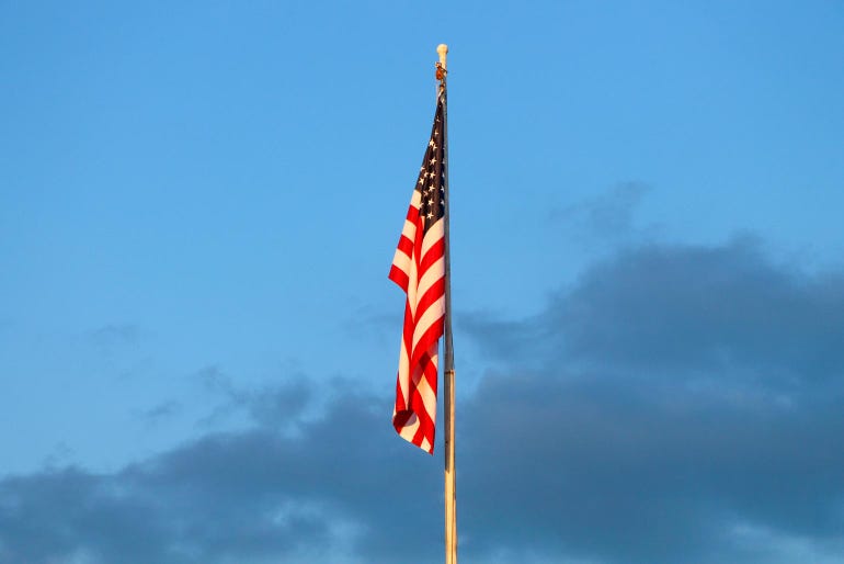 A close up of the American flag flying high during a sunset