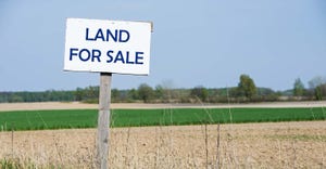 Land for sale sign in front of farm fields
