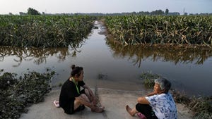Two women sitting next to flooded corn field