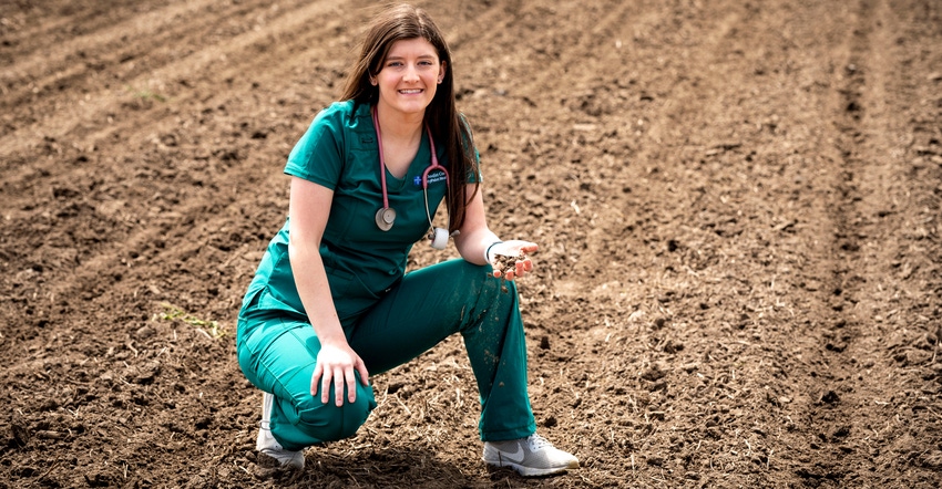Sophie Corkill in scrubs kneeling in a field